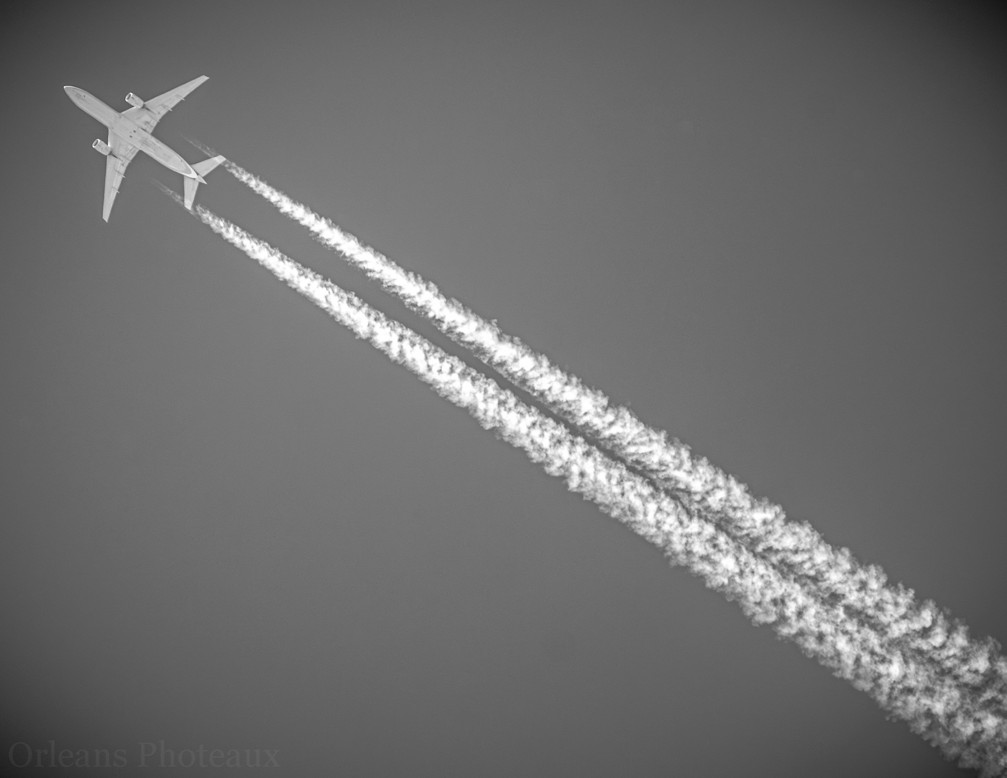 Black-and-white aircraft crossing overhead with long vapor trails