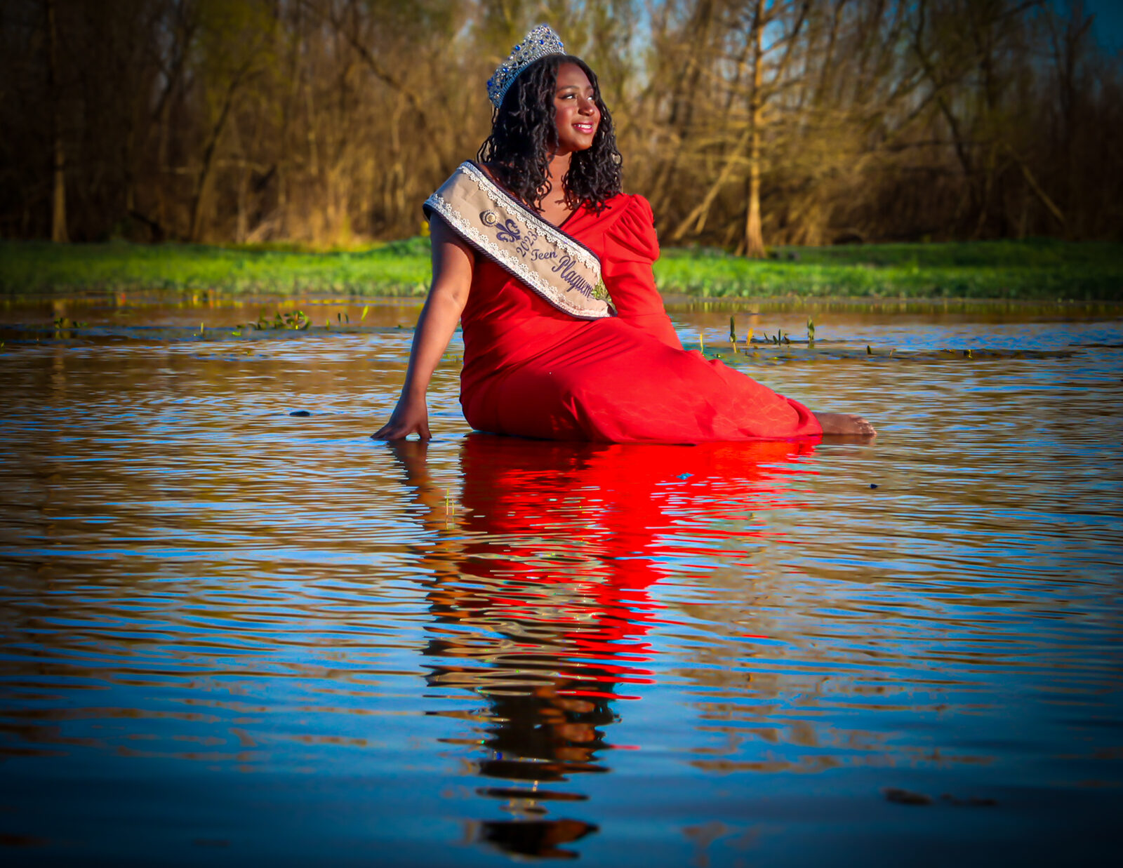 A pageant queen in a red gown photographed in reflective water